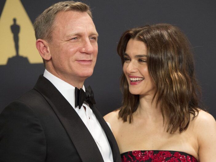Daniel Craig v smokingu se nasmehne poleg Rachel Weisz in se smeji v črno-rdeči obleki