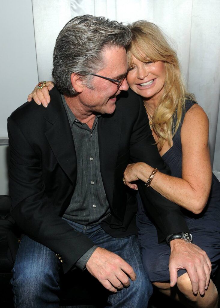 Goldie Hawn i en grå kjole legger armen rundt Kurt Russell i mørk dress og jeans
