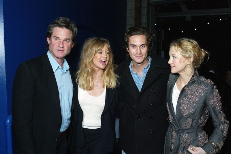 Kurt Russell (obleka), Goldie Hawn (obleka za hlače), Oliver Hudson (obleka) in Kate Hudson (siva obleka) se nasmehnejo drug drugemu