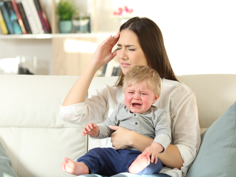 Mor lider og baby gråter desperat sittende på en sofa i stua hjemme