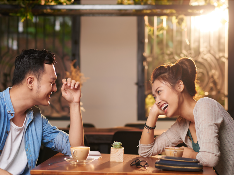 Portrets no sāniem, smejošs Āzijas pāris, kas bauda randiņu kafejnīcā