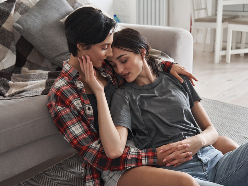 lesbisk lgbtq-par forelsket dating slapper av hjemme sammen sitter på gulvet og klemmer nyter et intimt ømt sensuelt øyeblikk, binding, chilling i leiligheten.