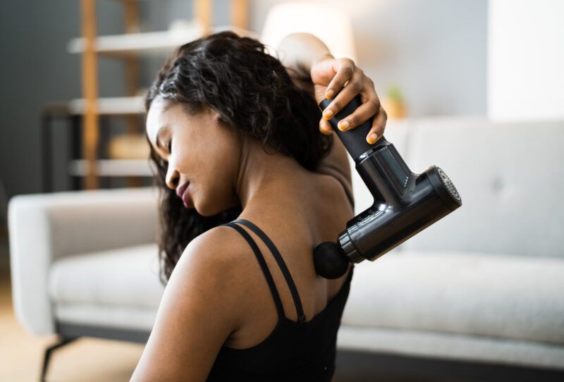 Mujer que usa una pistola de masaje para aliviar el dolor de espalda.