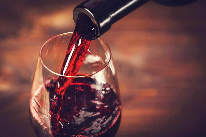 Puidust taustal punase veini klaasi valamine