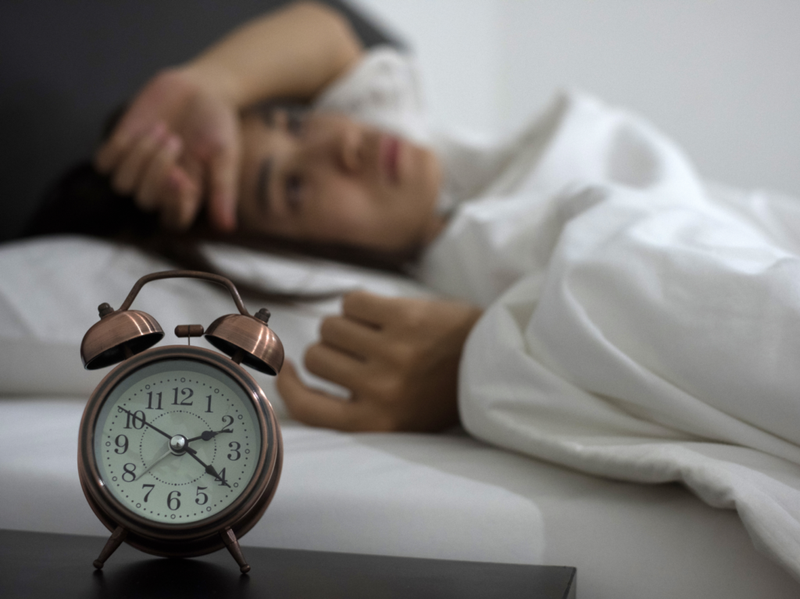 En kvinne ligger i sengen og klarer ikke å sove mens en vekkerklokke sitter ved siden av henne