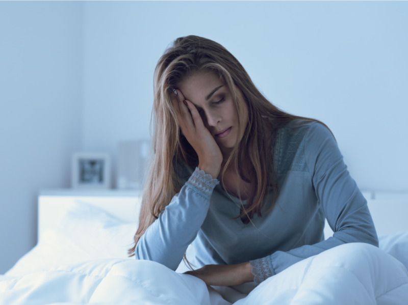 En kvinne setter seg opp i sengen og gnir seg i ansiktet etter en natt med dårlig søvn